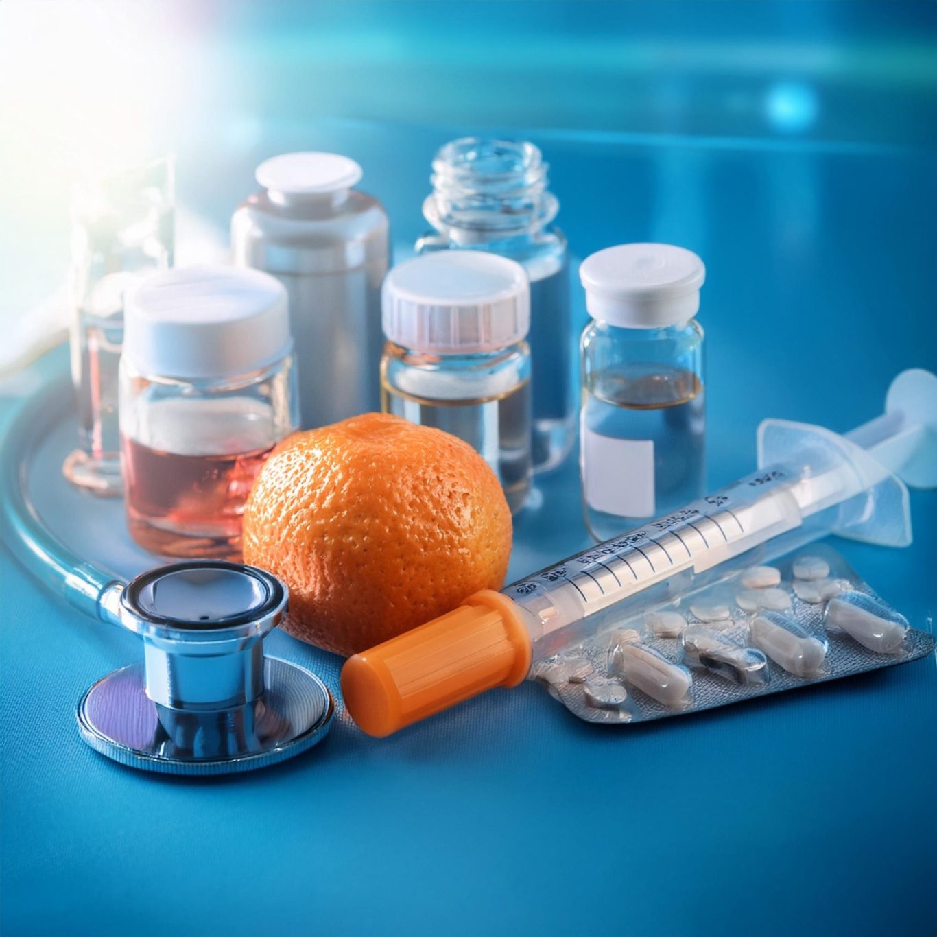 Endokrinologie: Bild mit Stethoskop, einer Spritze, Tabletten, mehreren Gläschen mit einer klaren Flüssigkeit und einer Mandarine